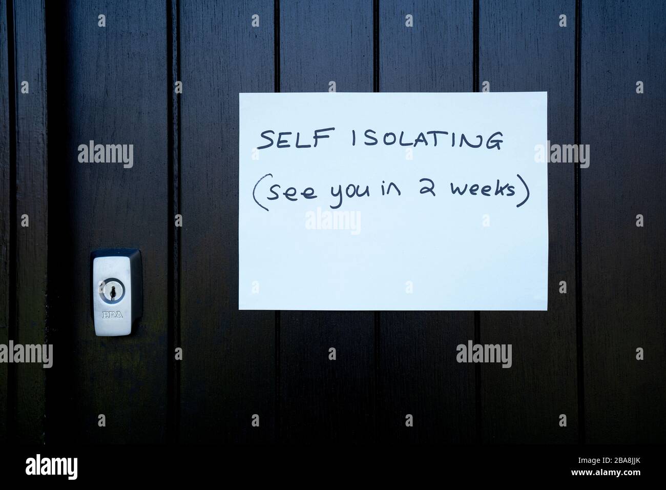 Handwritten self Isolation notice on black front door due to Coronavirus pandemic. Stock Photo