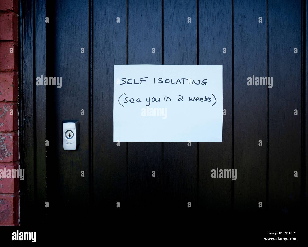 Handwritten self Isolation notice on black front door due to Coronavirus pandemic. Stock Photo