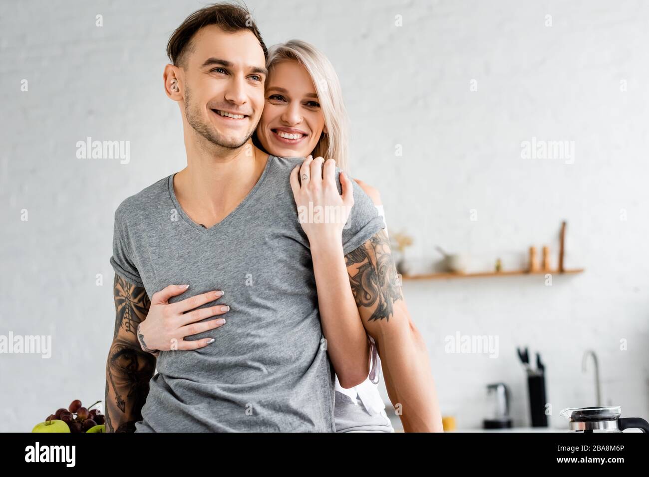 Smiling girl hugging tattooed boyfriend in kitchen Stock Photo - Alamy