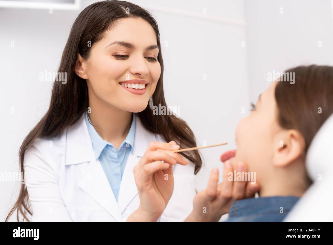selective focus of smiling otolaryngologist examining throat of kid