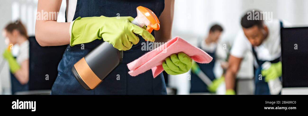 cropped view of cleaner in uniform spraying detergent on rag, panoramic ...