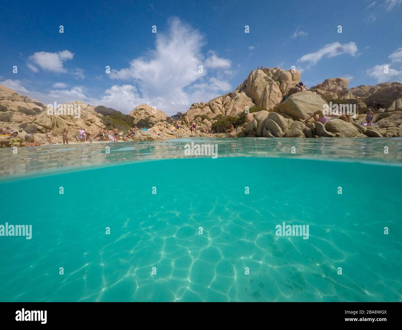Cala Coticcio, Sardinia, Italy – September 8, 2017: View over and under water surface, rocks with people and blue sky, mediterranean sea, split by wat Stock Photo