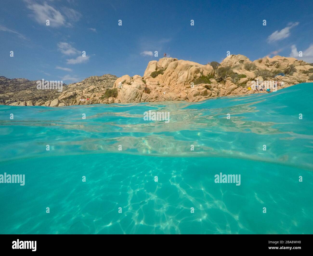 Cala Coticcio, Sardinia, Italy – September 8, 2017: View over and under water surface, rocks with people and blue sky, mediterranean sea, split by wat Stock Photo