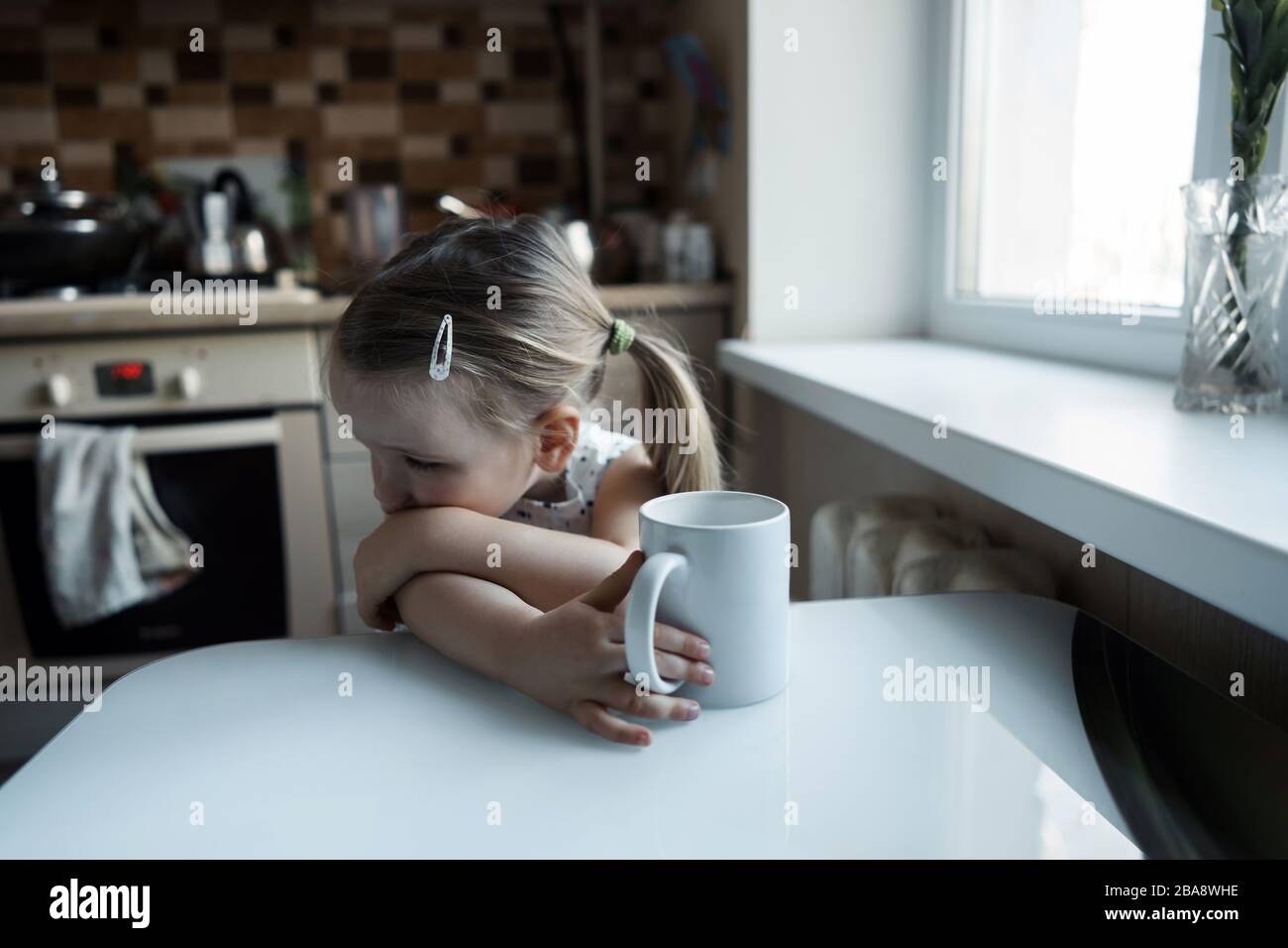 Little cute girl sitting at the table in the kitchen Stock Photo