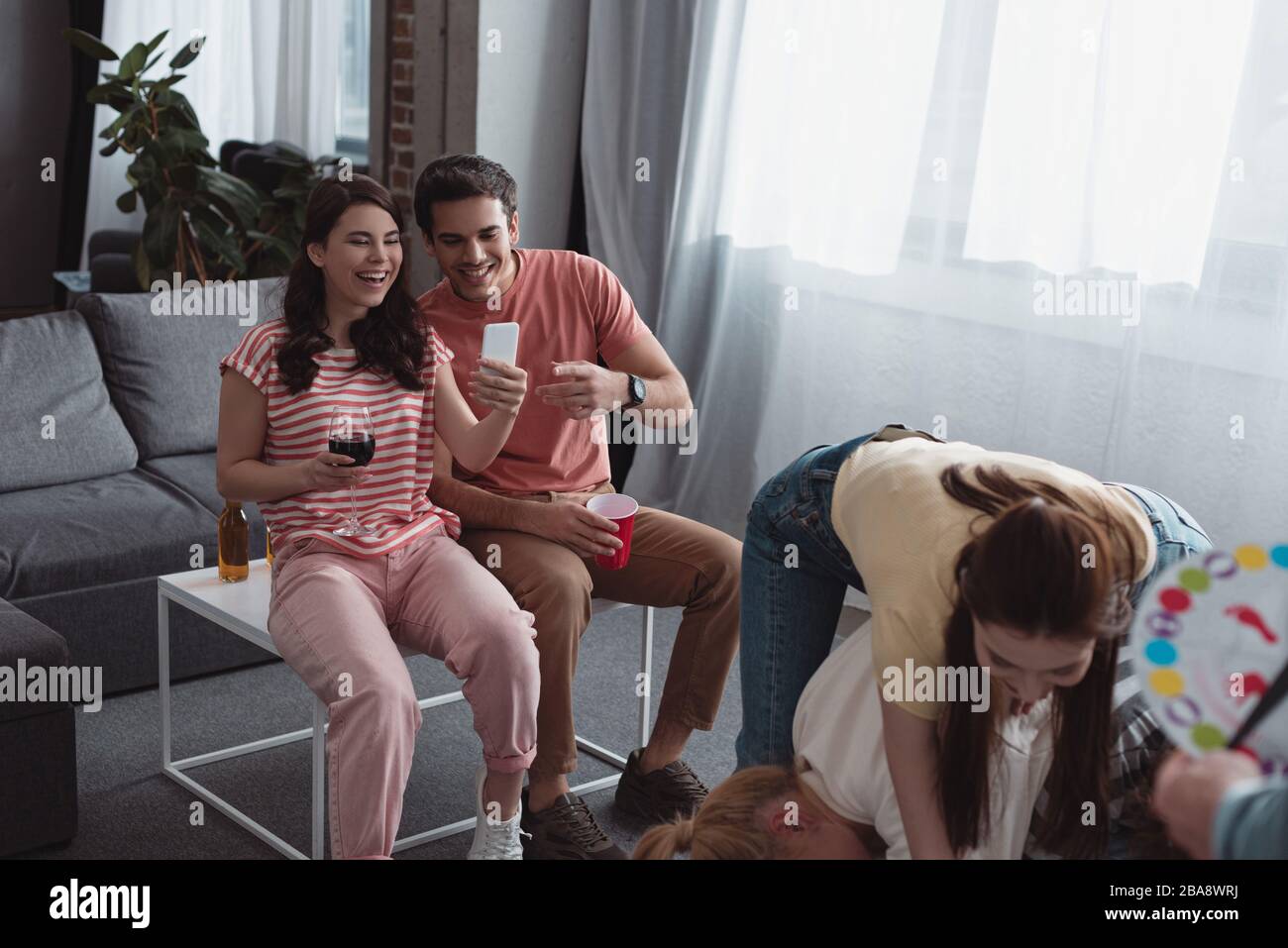 KYIV, UKRAINE - JANUARY 27, 2020: smiling girl taking photo of friends playing twister game Stock Photo