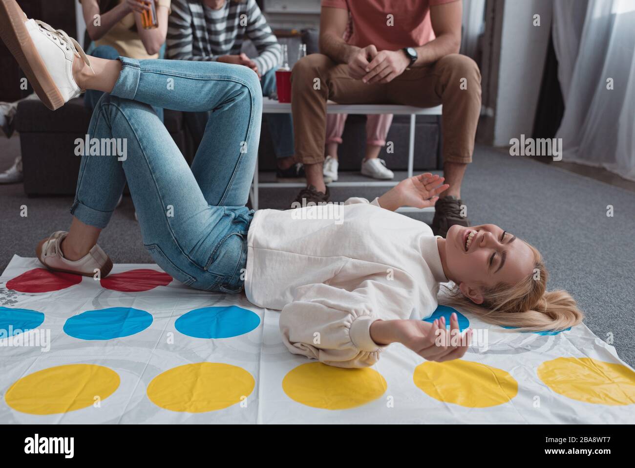 KYIV, UKRAINE - JANUARY 27, 2020: cheerful girl smiling while lying on twister game mat near friends Stock Photo