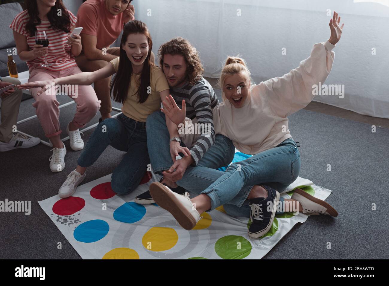 KYIV, UKRAINE - JANUARY 27, 2020: high angle view of friends sitting on twister game mat while others resting on sofa Stock Photo