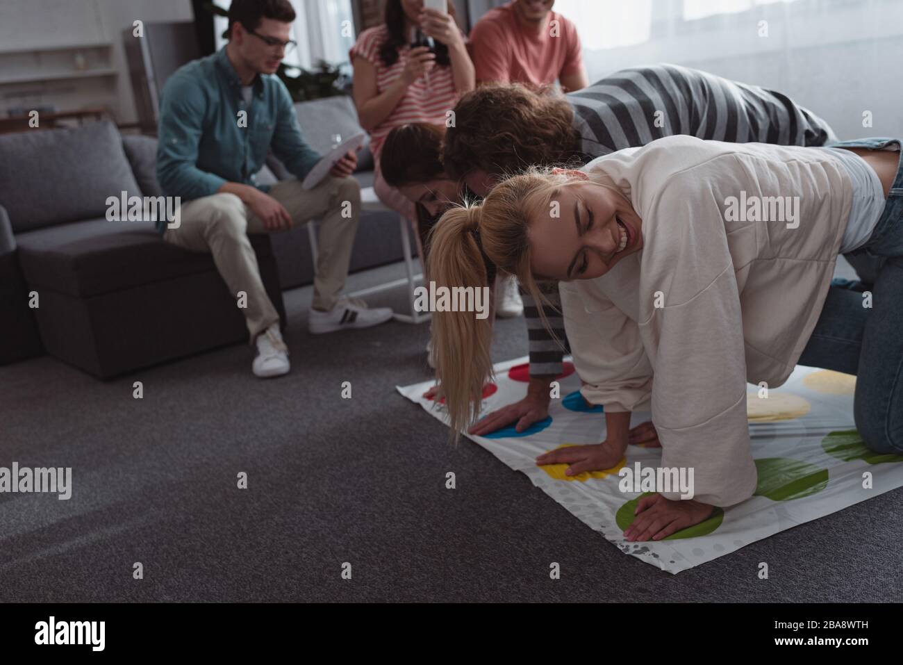 KYIV, UKRAINE - JANUARY 27, 2020: cheerful friends playing twister game while others resting on sofa Stock Photo