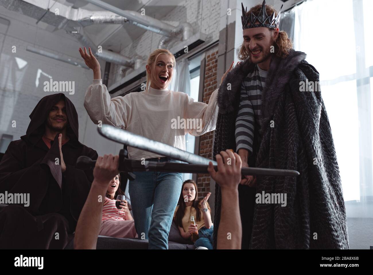 men in costume of king fighting with knight with toy swords near friends Stock Photo