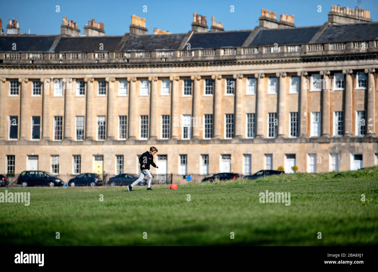 A young boy plays football in front of the Royal Crescent in Bath, after the UK government introduced strict restrictions in a bid to combat Coronavirus. Stock Photo