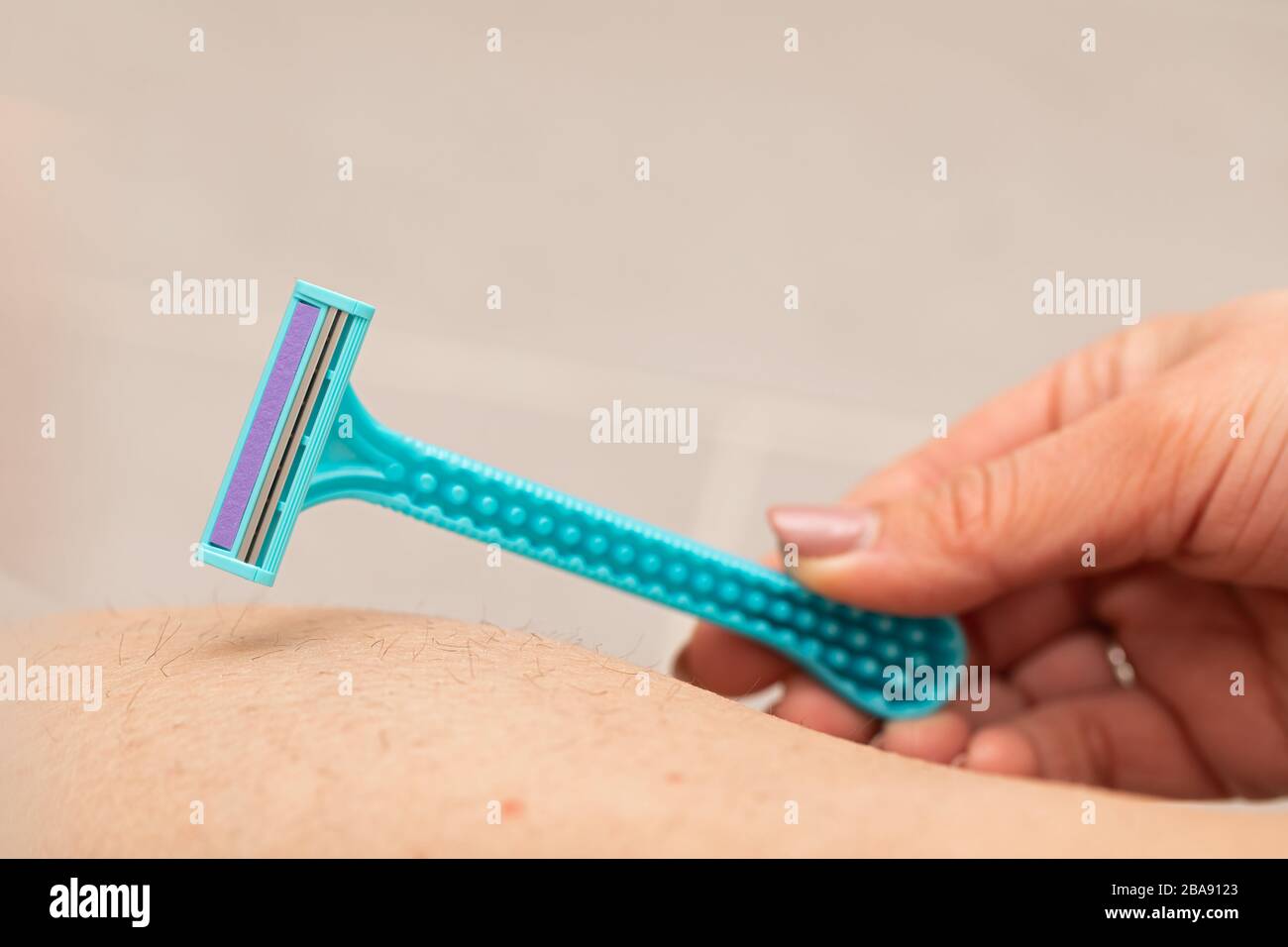 Close up picture of woman holding razor, shaving her hairy leg with ...