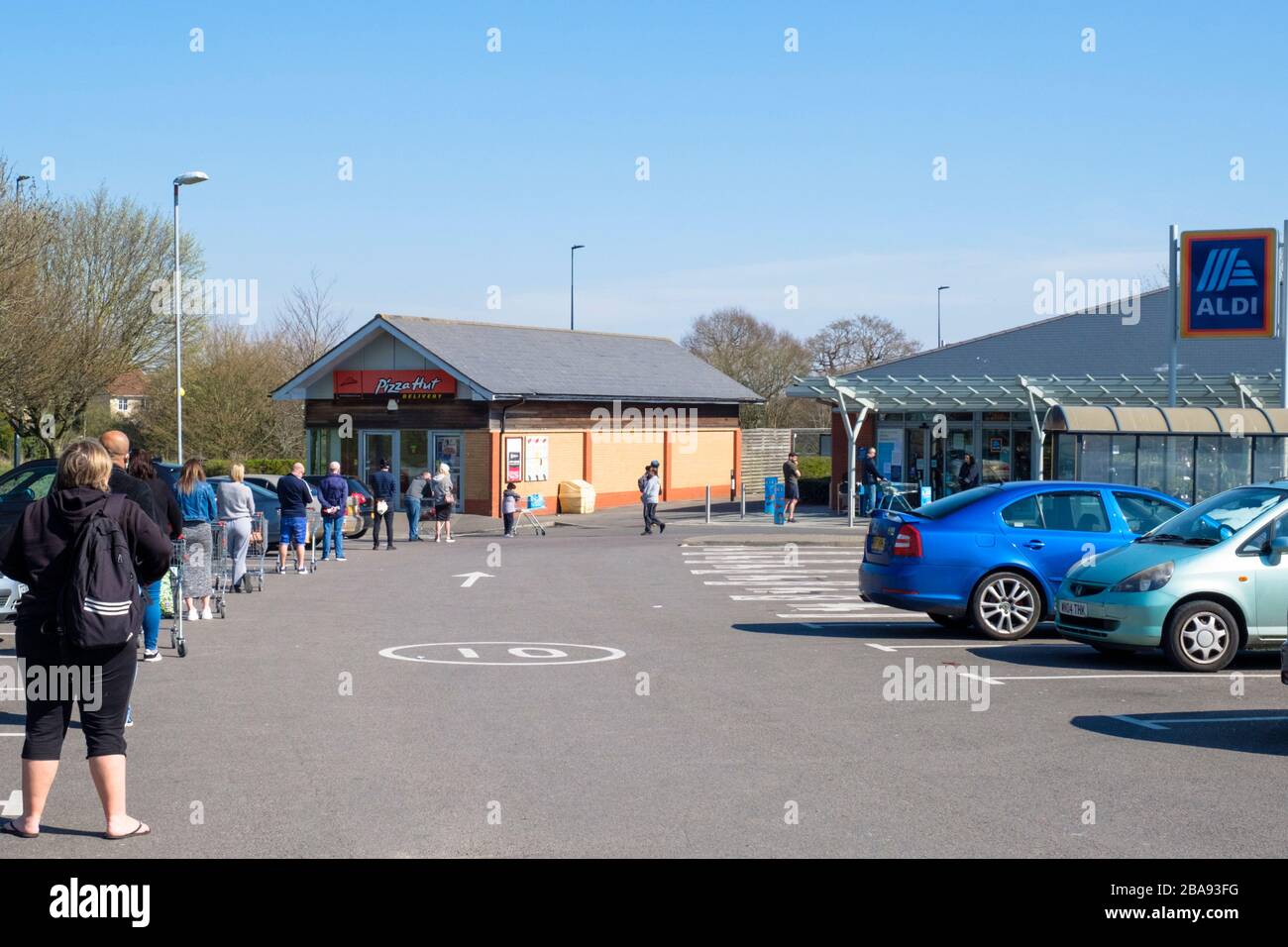 Bradley Stoke, Gloucestershire, UK, 26th March 2020. On day3 of the Corvid 19 lockdown in the UK a  long queue forms for the ALDI supermarket in Bradley Stoke. Shoppers comply with social distancing rules by standing 2 or more metres apart.  Credit: Mr Standfast / Alamy Live News Stock Photo