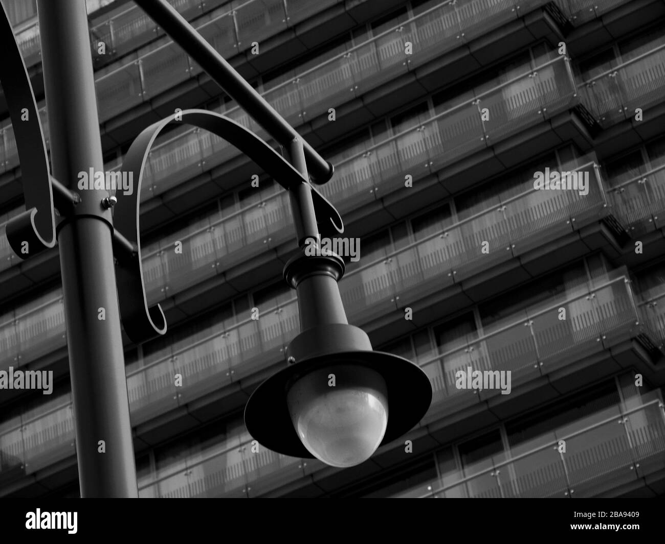 view of old vintage style street lamps on skinny tall steel posts and large glass lens covers and stylish glass exterior corridors of hotel building Stock Photo