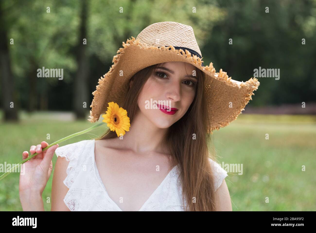 Young attractive girl holds a summer wildflower. She enjoys nature, the smell of flowers, outdoor recreation. Stock Photo