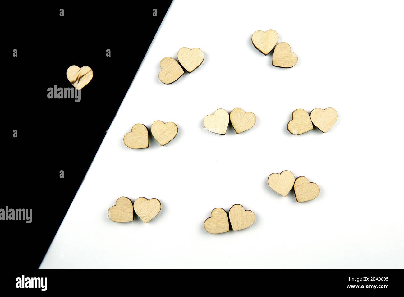 A lot of wooden hearts placed by couples on white background and one on black background. Concept of love and loneliness, isolation. Flat lay. Stock Photo