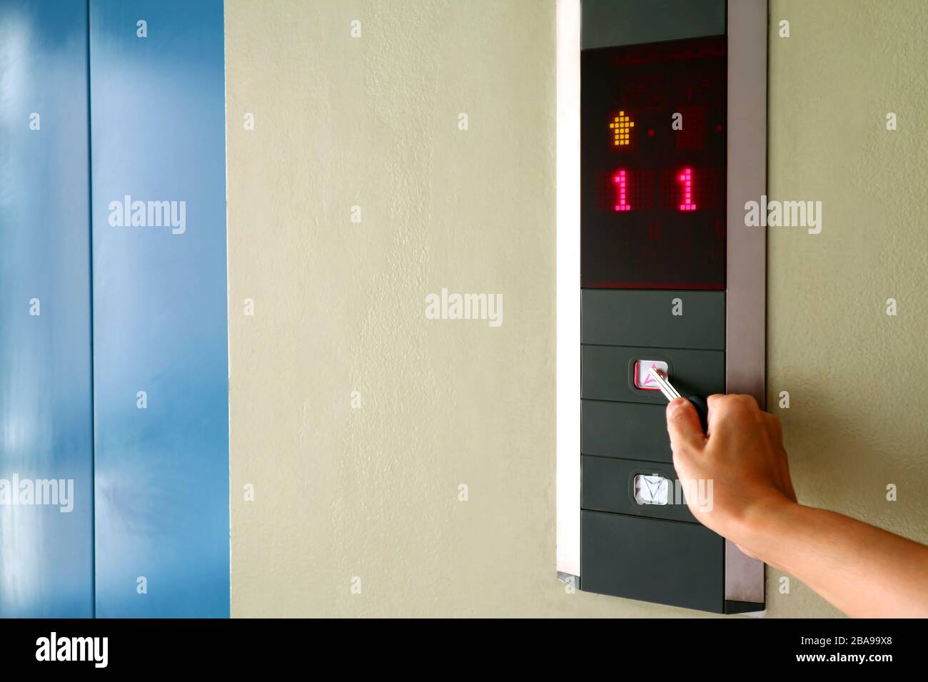 Hand pressing the button of elevator with key for self-sanitization Stock Photo