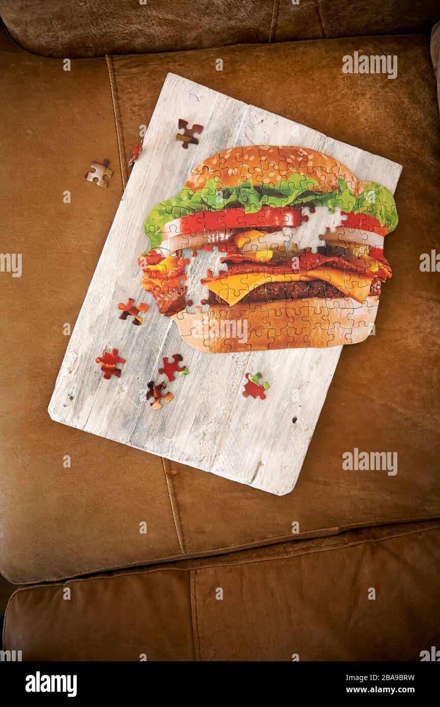 Cheeseburger jigsaw un finished on a white chopping board on a brown leather sofa Stock Photo