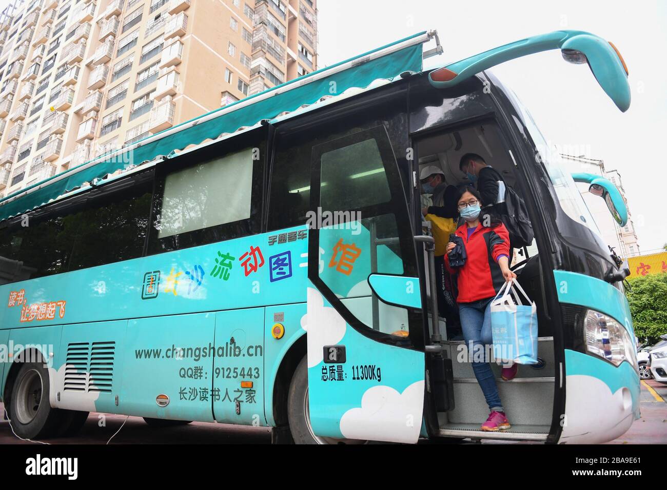 Changsha, China's Hunan province. 26th Mar, 2020. A woman leaves the mobile library with borrowed books in a community of Changsha, central China's Hunan province, March 26, 2020. Recently, the mobile libraries in Changsha have resumed operation amid epidemic prevention and control measures. Mobile library is a project of Changsha Library which takes buses as carriers to visit communities, schools, companies, construction sites and other areas in the city monthly and provide book reading, consulting, borrowing and returning services. Credit: Chen Zeguo/Xinhua/Alamy Live News Stock Photo