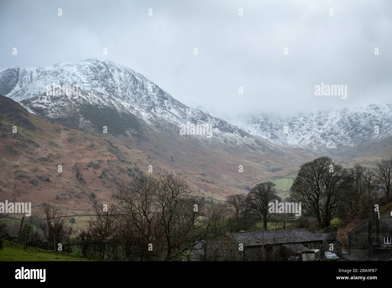Looking up Greenburn, Little Langdale, to the snow covered summit of Wetherlam with clouds covering the summits of Swirl How and Great Carrs,  Lake Di Stock Photo