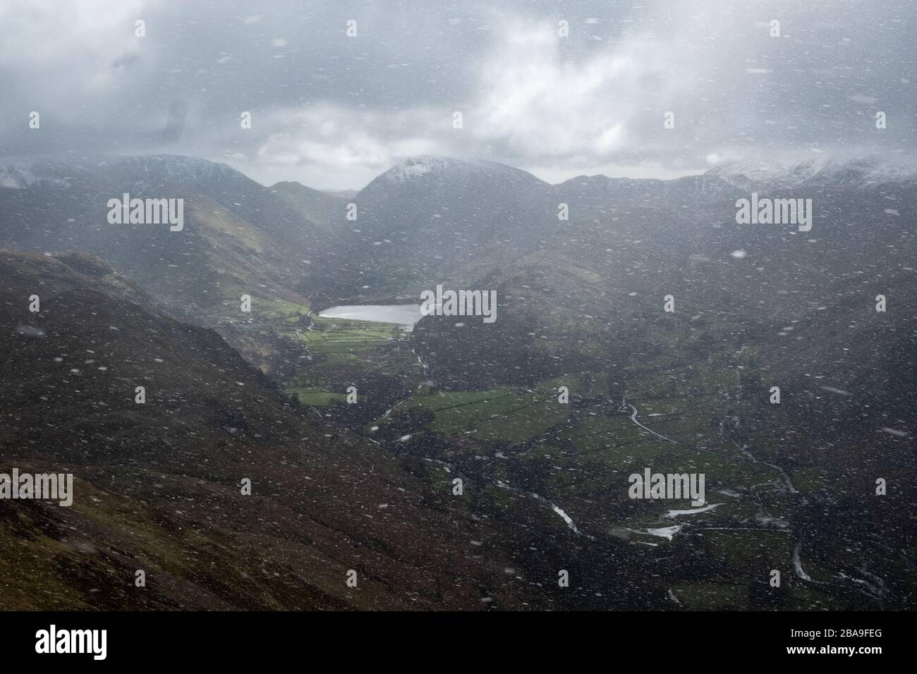 View thorugh falling snow to Brothers Water and Patterdale on the descent from Place Fell, Lake District, UK Stock Photo