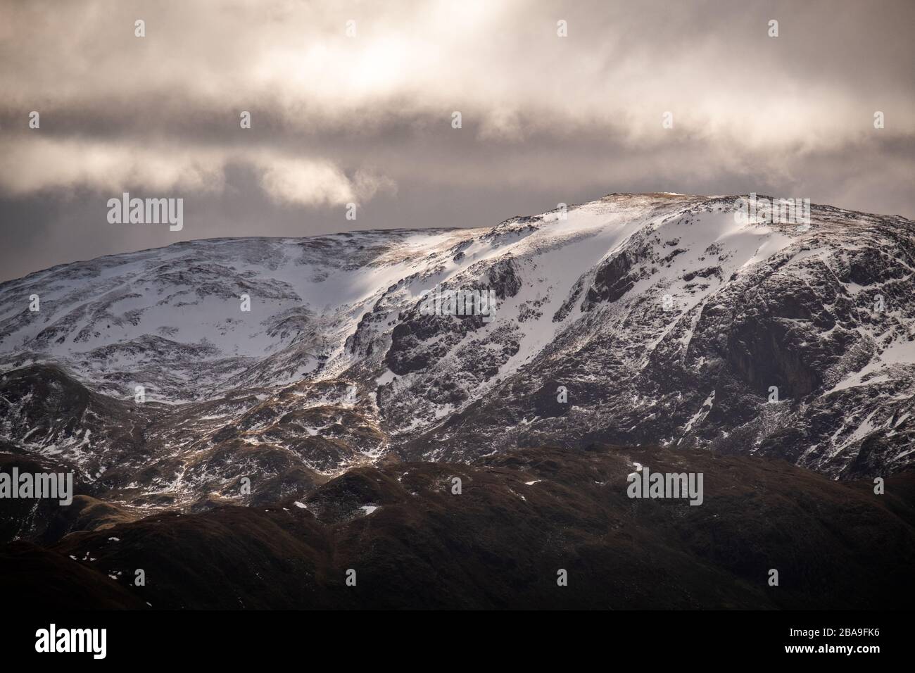 Close up of sun breaking through clouds on the snow covered Eastern Face of Dolywaggon Pike, Lake District, UK Stock Photo