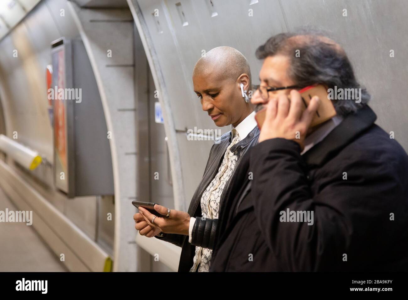A woman uses her smartphone on the Underground while a man makes a phone call, part of the London Underground subway system Stock Photo
