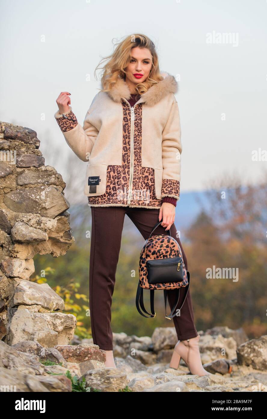 Natural wool sheepskin coat. Fur on hood. Hit of season. Stay warm and fashionable. Woman wear furry coat. Winter clothes. Wardrobe for cold weather. Girl stand near stone ruins. Fancy chic coat