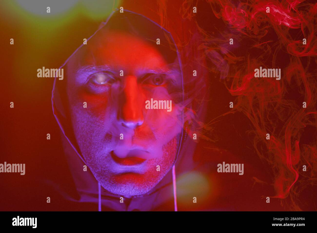 A man in a mask and chemical protection suit in red and blue light. Fight against the virus Stock Photo