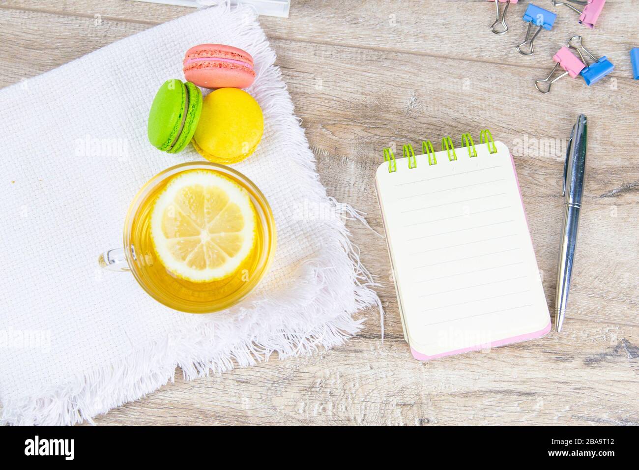 An open notebook with a silver pen, a cup of mint tea with lemon and multi-colored muffins stand next to it Stock Photo
