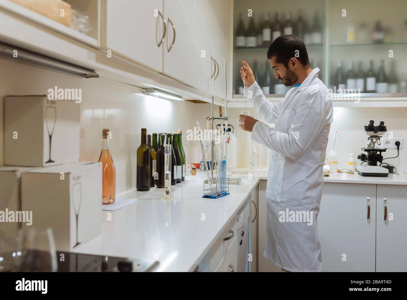 Arabic winemaker working in winelab wearing white gown and gloves. Stock Photo