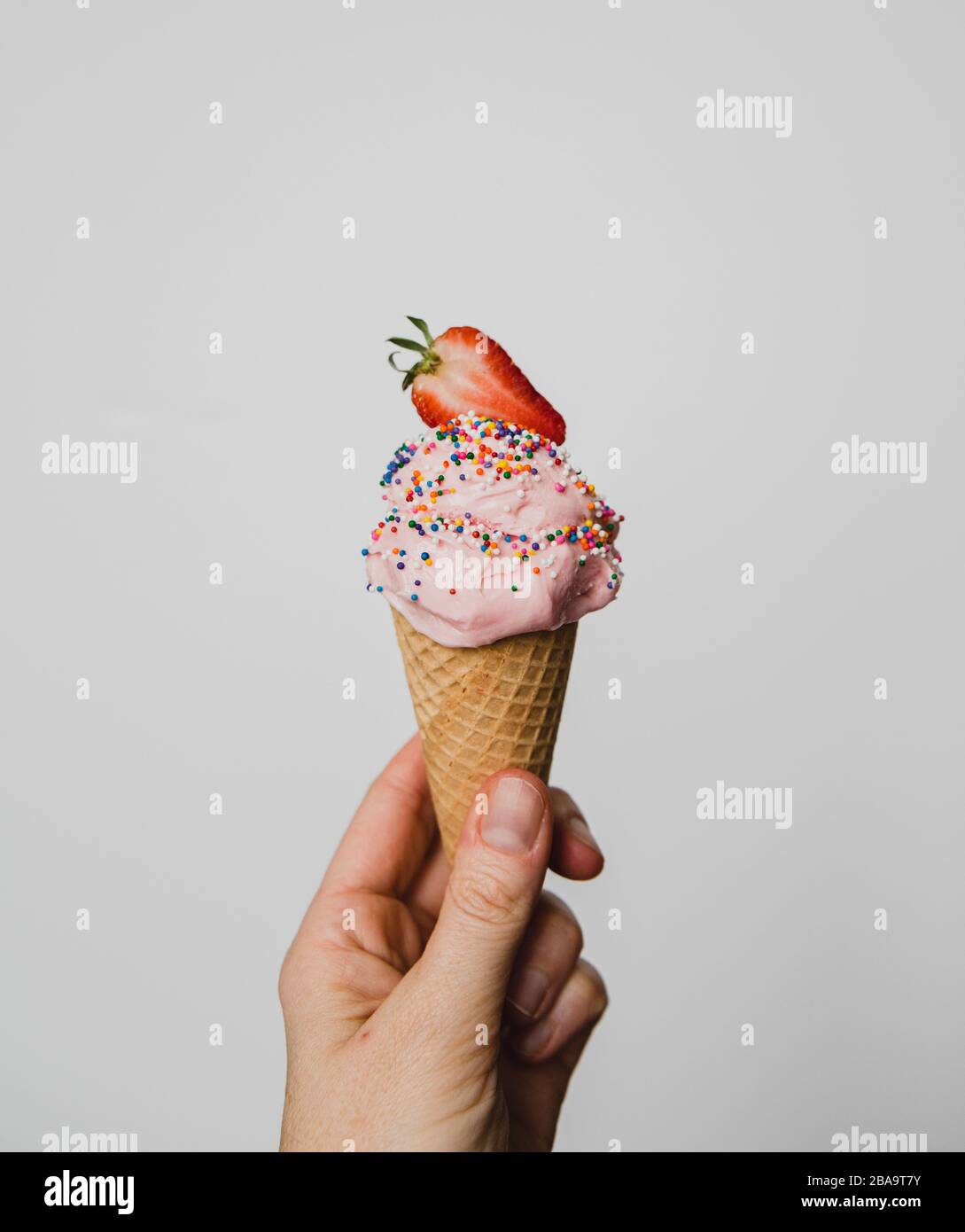 Hand holding strawberry ice cream cone against white background. Stock Photo