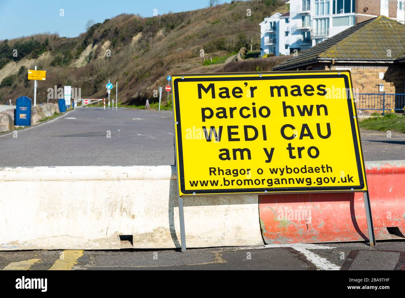 An empty seaside car park behind a temporary barrier with Welsh language sign due to social distancing restrictions during coronavirus crises. Stock Photo