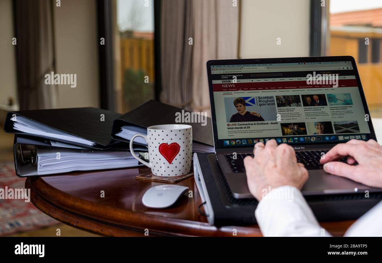Woman working on laptop on table at home with screen showing BBC Scotland news website with Nicola Sturgeon and Covid-19 Coronavirus pandemic Stock Photo