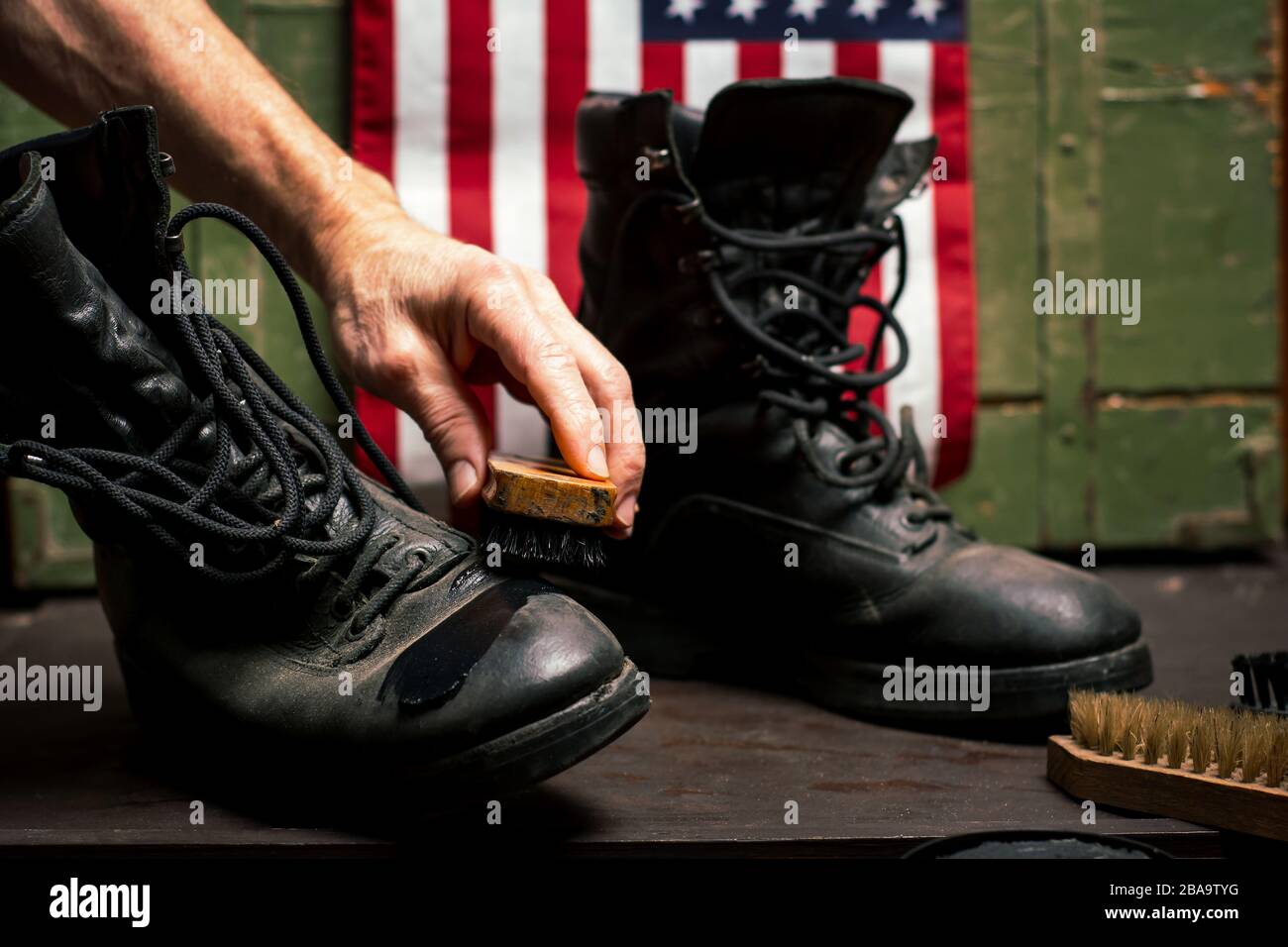 Man polishing vintage military boots in front of USA flag Stock Photo