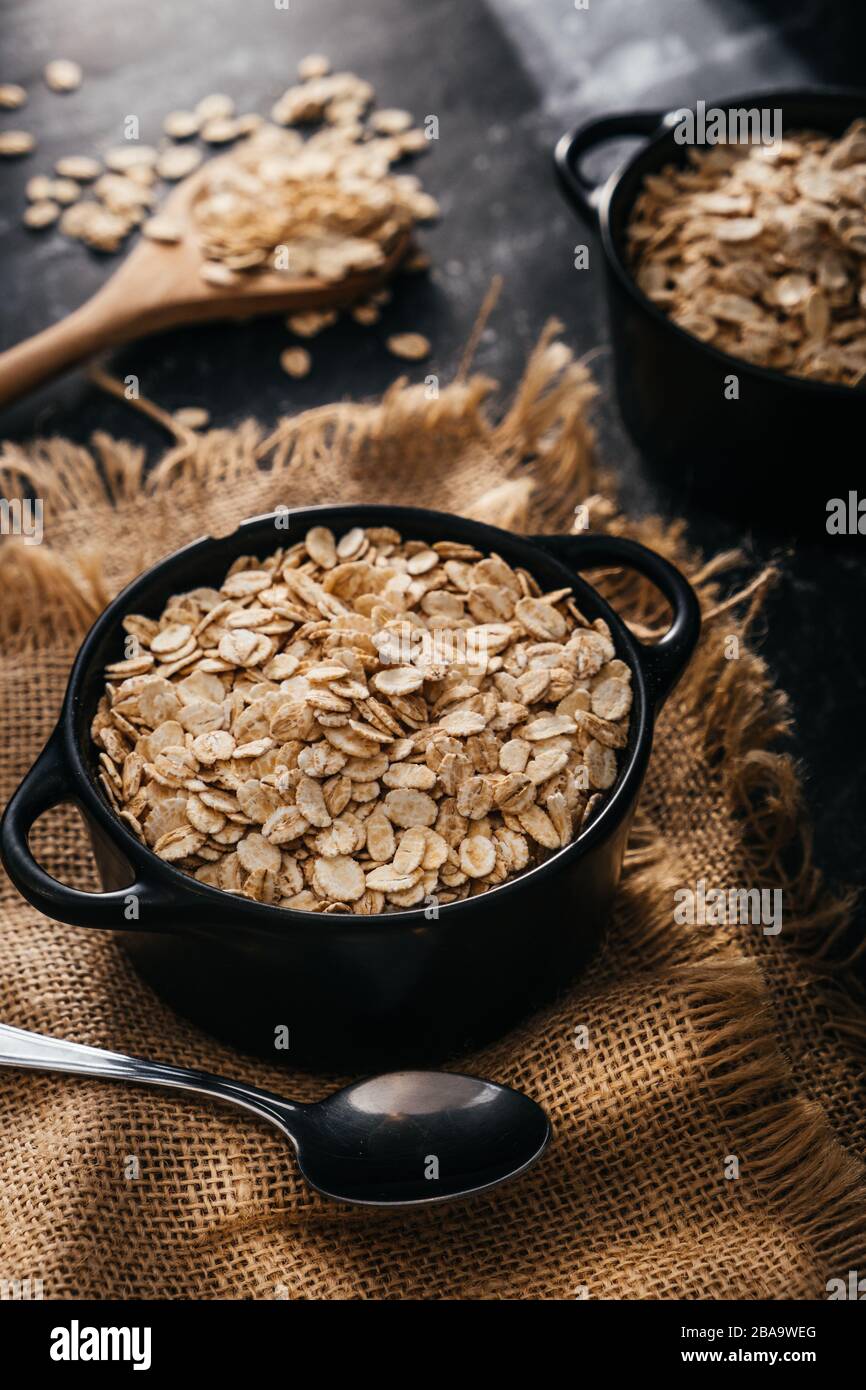 Top view of two black bowls and spoon with raw oatmeal on a black background. Breakfast with fibers for a balanced diet. Oat photo Stock Photo