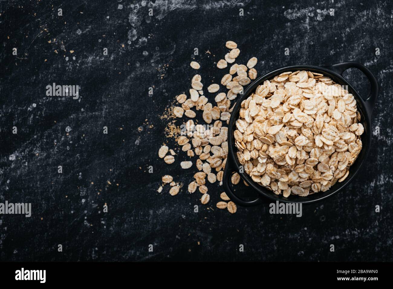 Top view of a black bowl with oat flakes on a black background. healthy food concept. The image has a space to place texts or logos Stock Photo