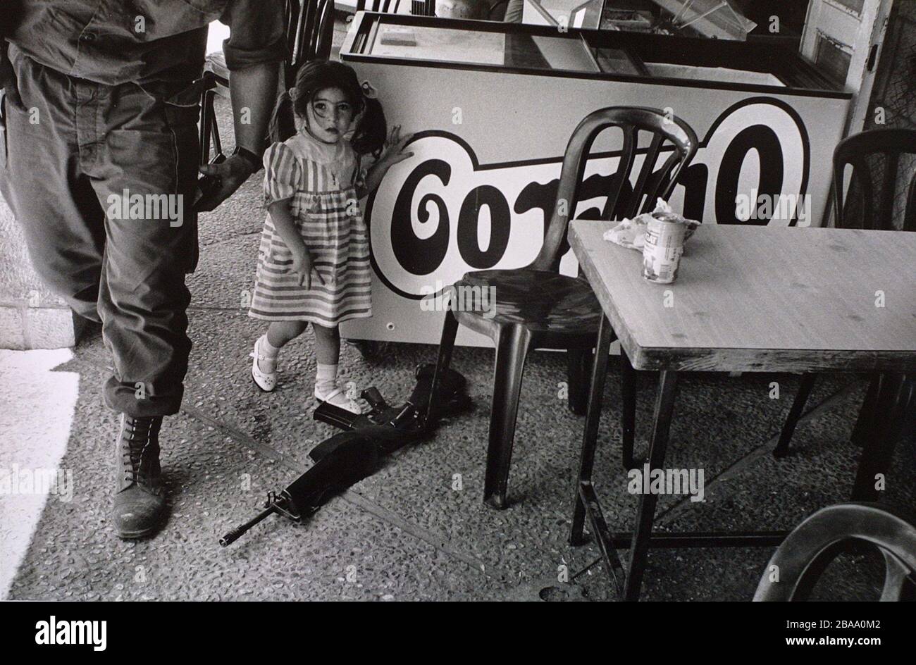 A young settler girl pointing to a gun belonging to a soldier from the Israel Defense Force (IDF) at a cafe in the West Bank settlement of Kiryat Arba near Hebron. In 1994 a settler named Baruch Goldstein shot dead 29 Palestinians in the nearby city of Hebron. Israel occupied the West Bank, Gaza and Golan Heights in the aftermath of the Six-Day-War of 1967. Stock Photo