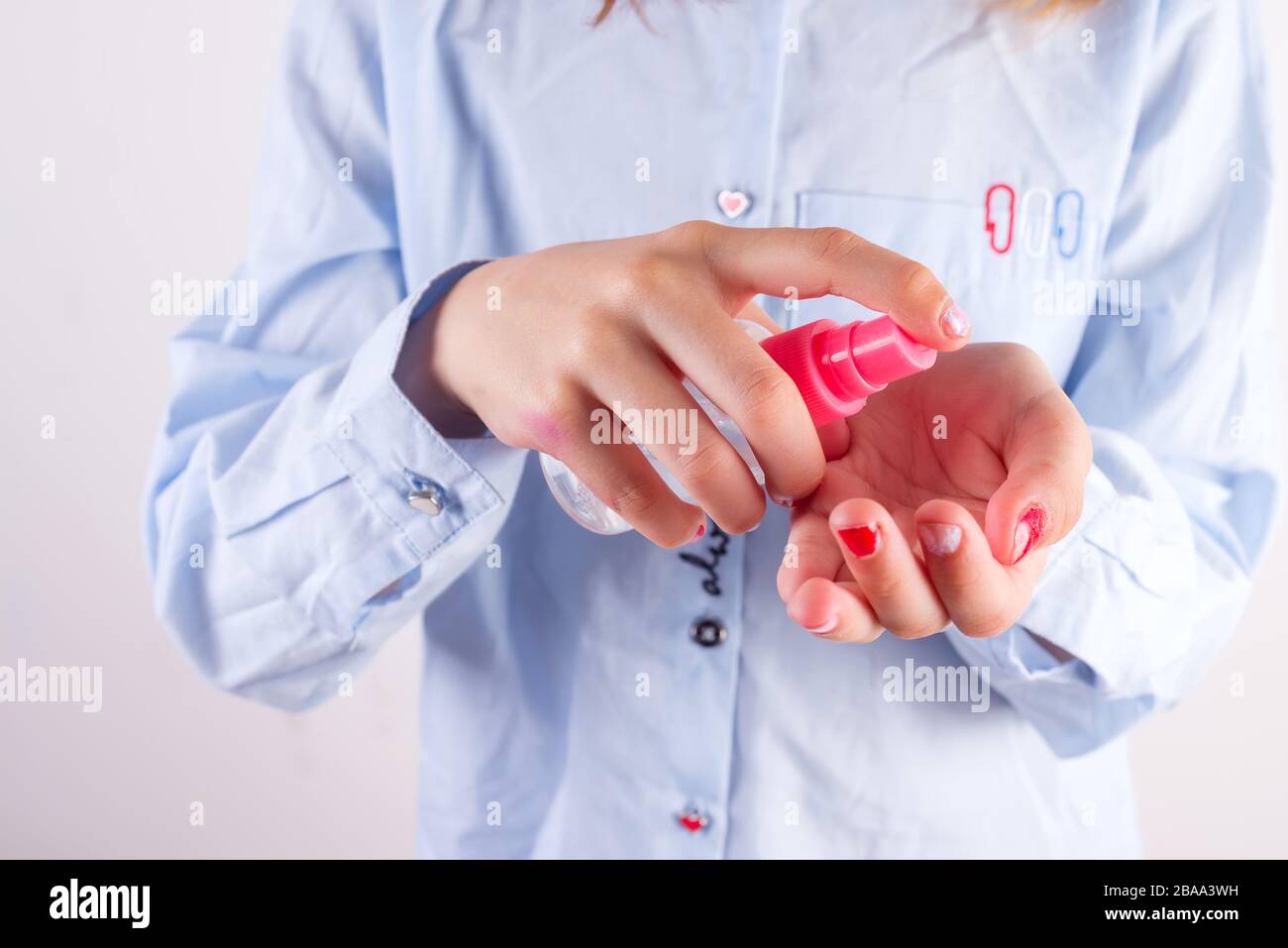 Close-up view girl in a pastel blue shirt is cleaning her hand by antiseptic liquid in a plastic bottle against light white background, copy space. Pr Stock Photo