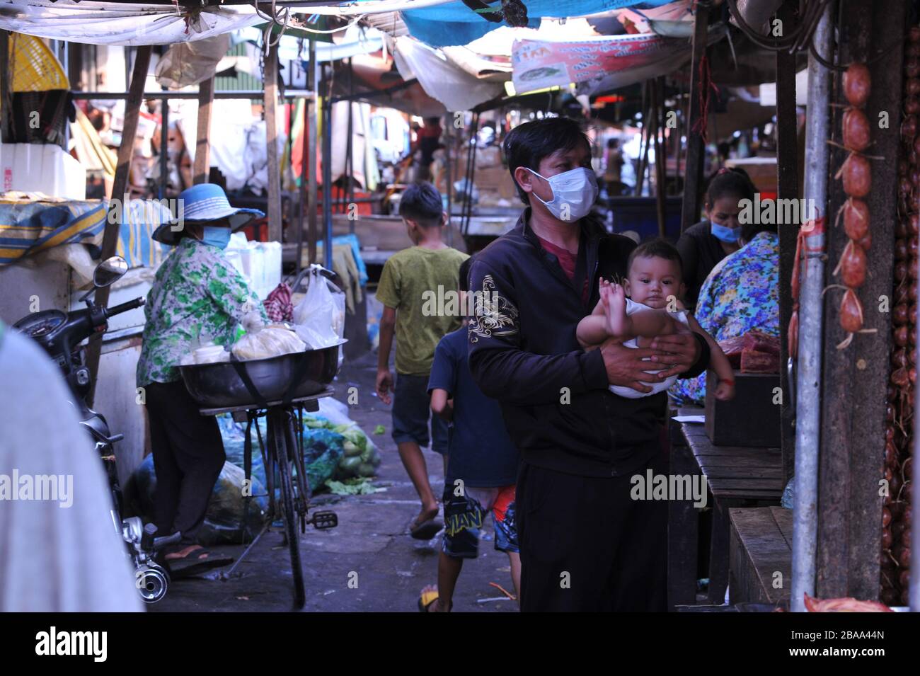 A Cambodian father, shopping & wearing a face mask, holds his baby