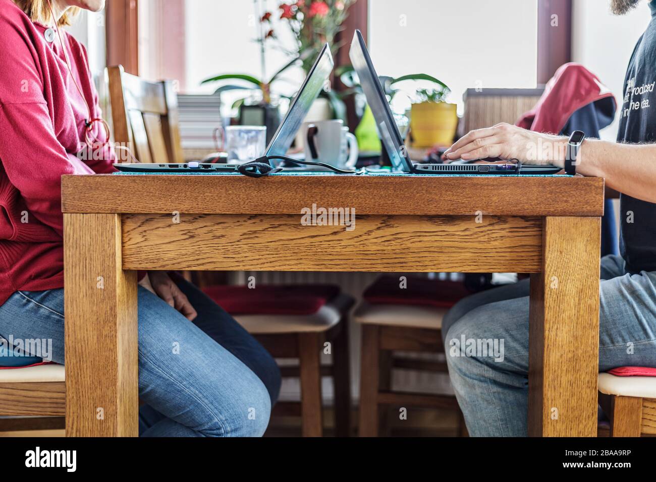 Couple working from home during coronavirus pandemic. Candid image of man and woman sitting at one table with their laptops and other stuff nearby. Stock Photo