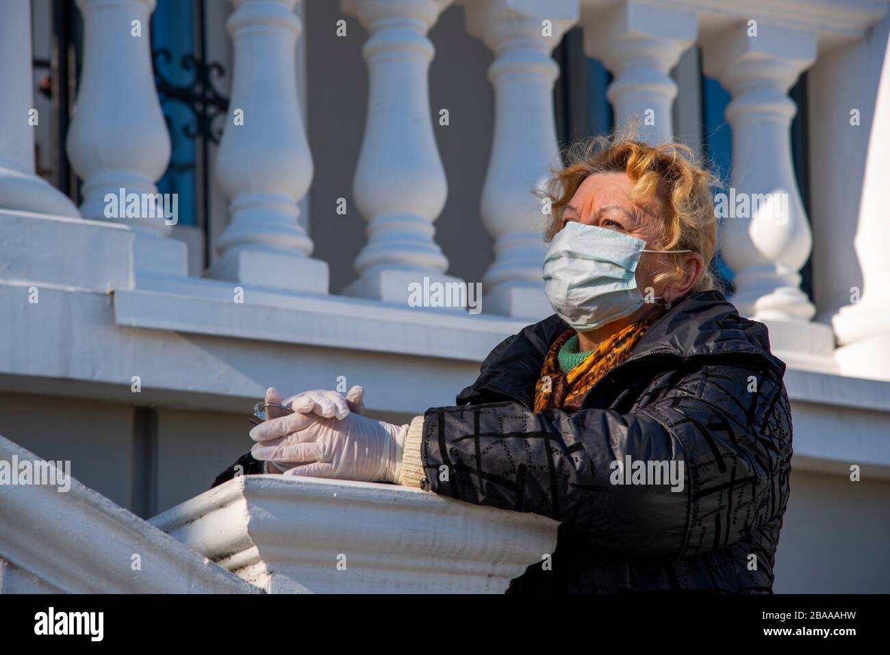 An elderly woman in rubber gloves and a protective mask stands against ...