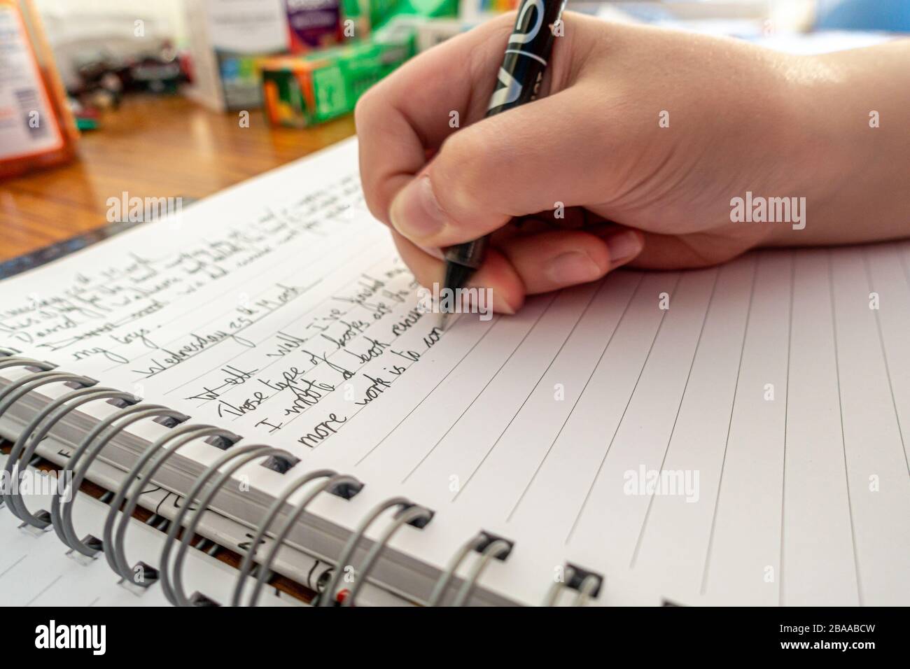 A young boy writes a diary of events during coronavirus lockdown as handwriting practice and to remember current events in the future. Stock Photo