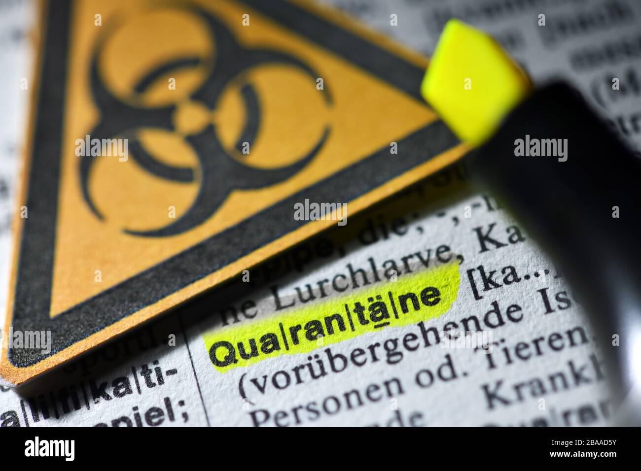 The word Quarantine in a dictionary and biology danger sign, symbolic photo Corona crisis, Das Wort Quarantäne in einem Wörterbuch und Biogefährdungsz Stock Photo