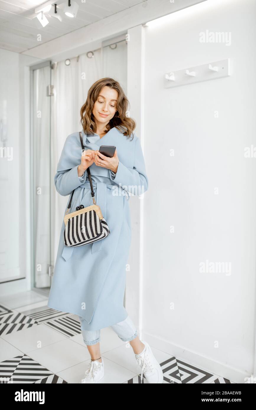 Young woman getting ready to leave the apartment, standing with handbag and mobile phone in the hallway Stock Photo
