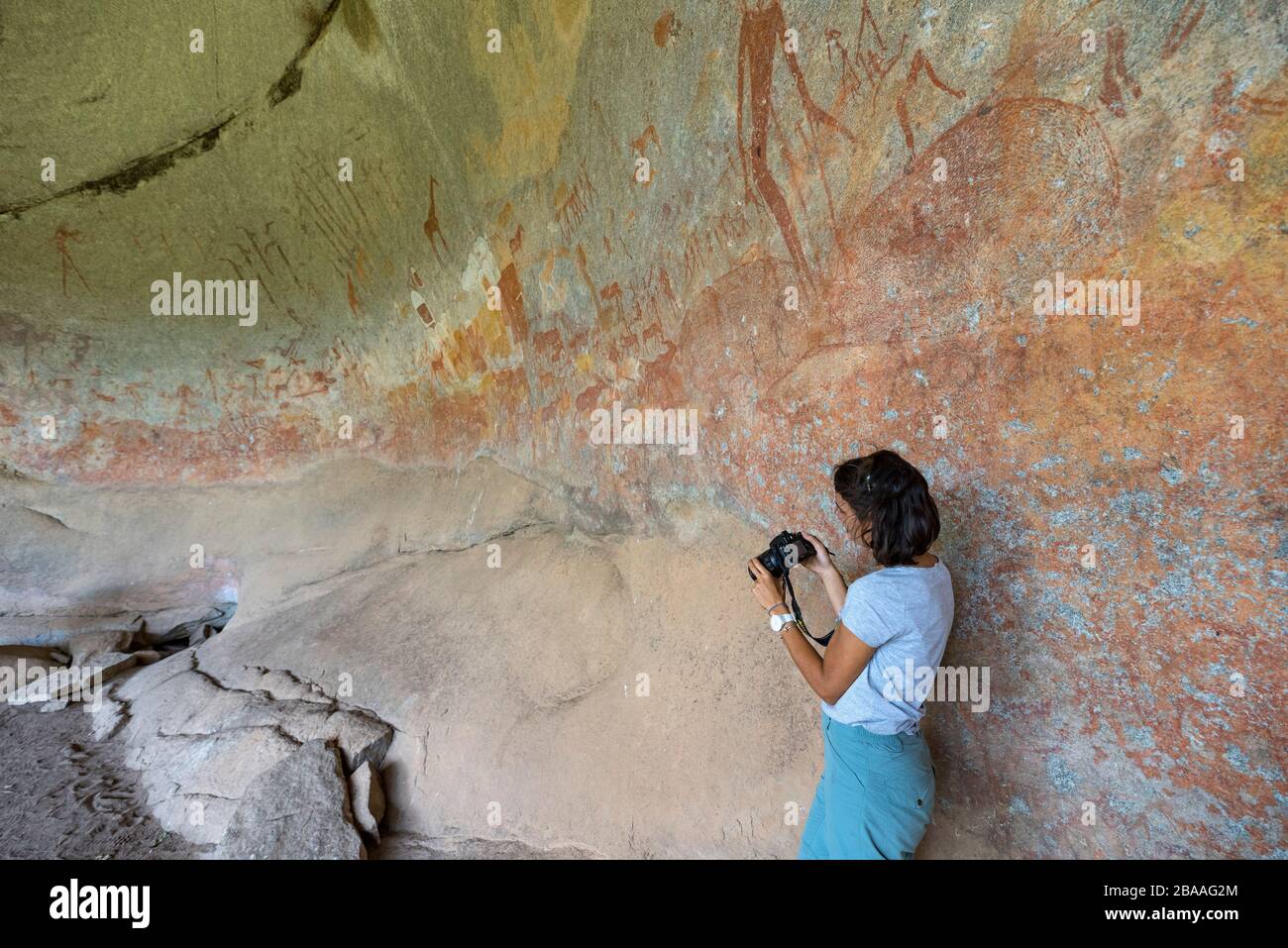 A tourist takes a photograph of the San rock art in Inanke Cave, Matobo National Park, Zimbabwe. Stock Photo