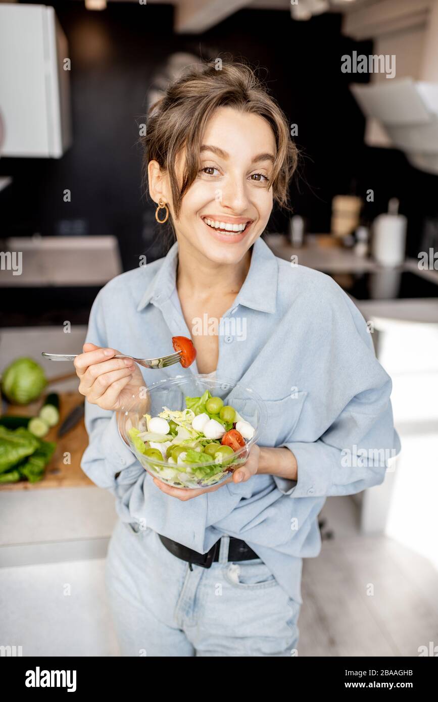 Portrait of a young and cheerful woman eating healthy salad on the kitchen at home. Healthy eating, food and lifestyle concept Stock Photo