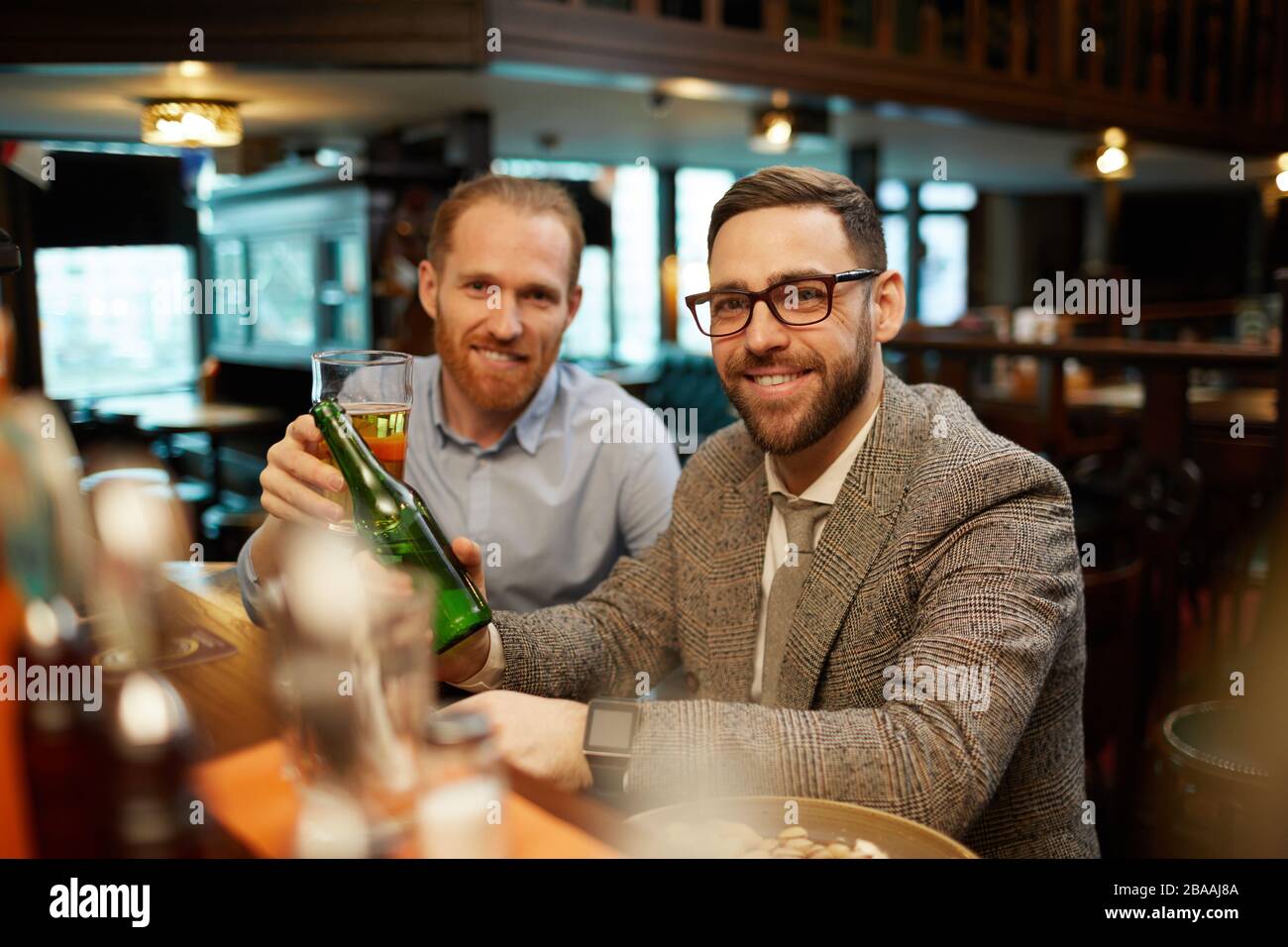 Portrait of two friends smiling at camera while drinking beer at bar counter in the bar Stock Photo