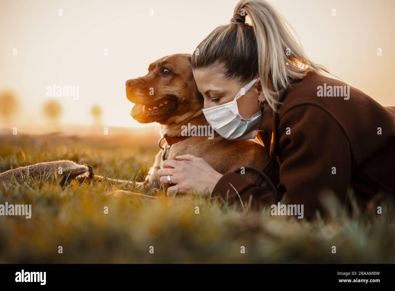 Woman wearing a protective mask is walking alone with a dog outdoors because of the corona virus pandemic covid-19 Stock Photo