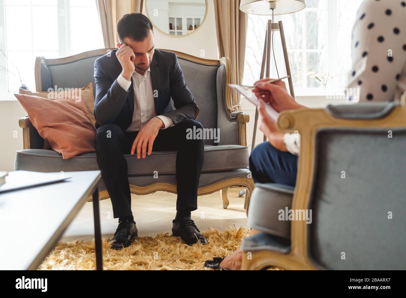 Low-spirited dark-haired man sitting on a sofa Stock Photo