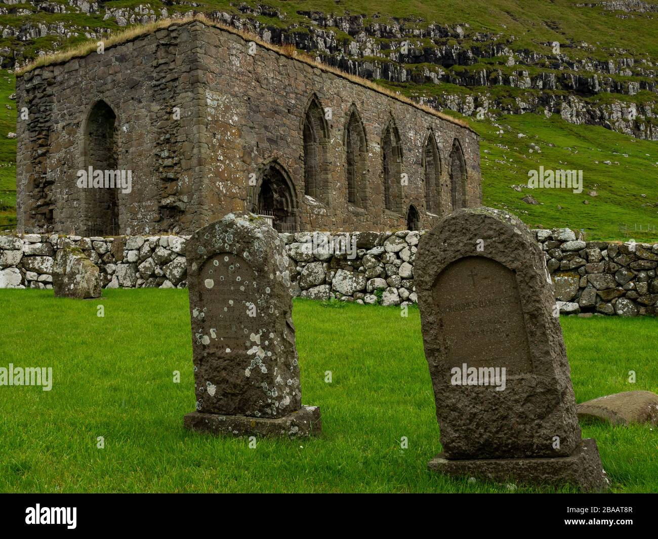 Faroe Islands. Kirkjubøur village. Old never roofed ruins of medieval cathedral. Gravestones in the old cemetery. Stock Photo